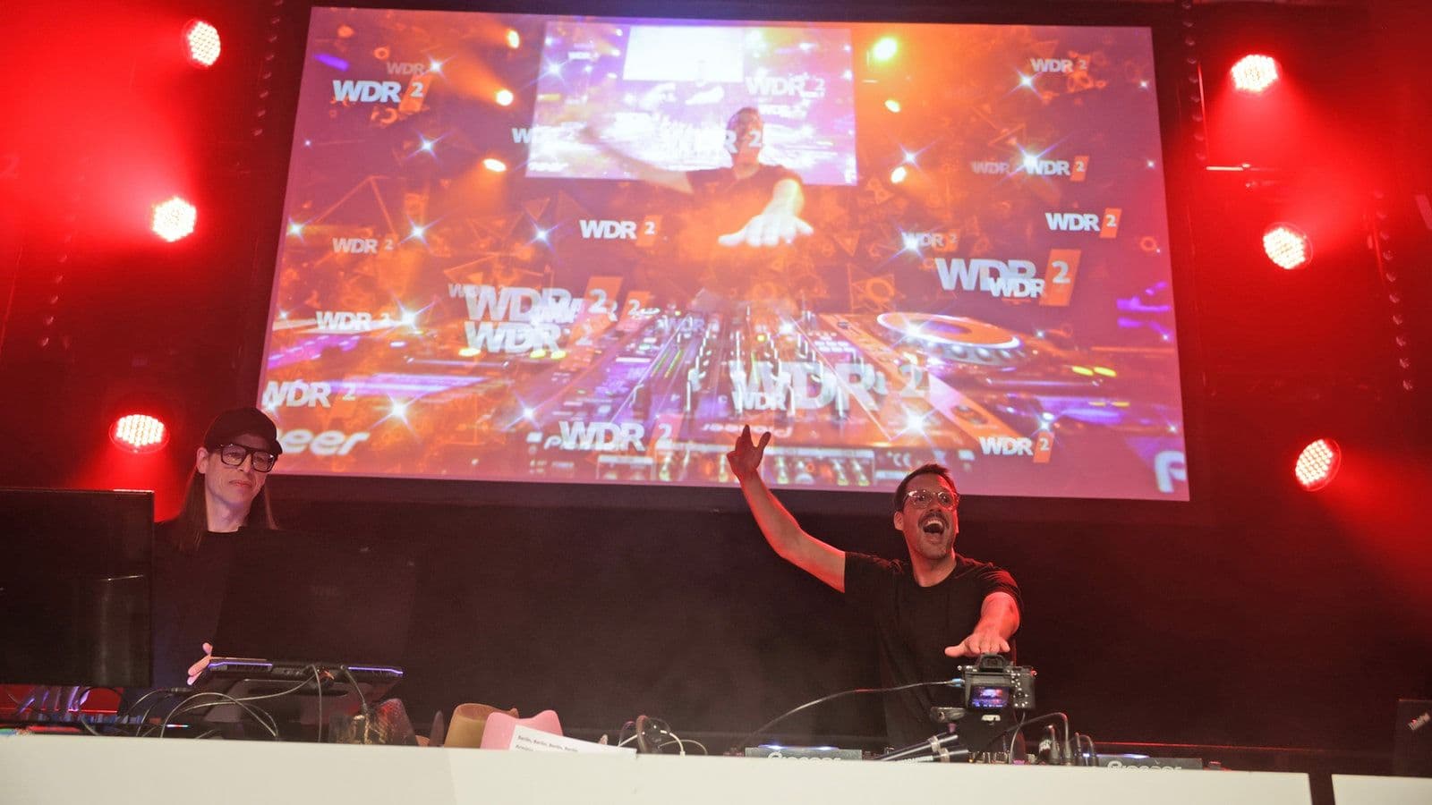 Ein DJ steht vor einer Leinwand auf der WDR 2-Hausparty.
