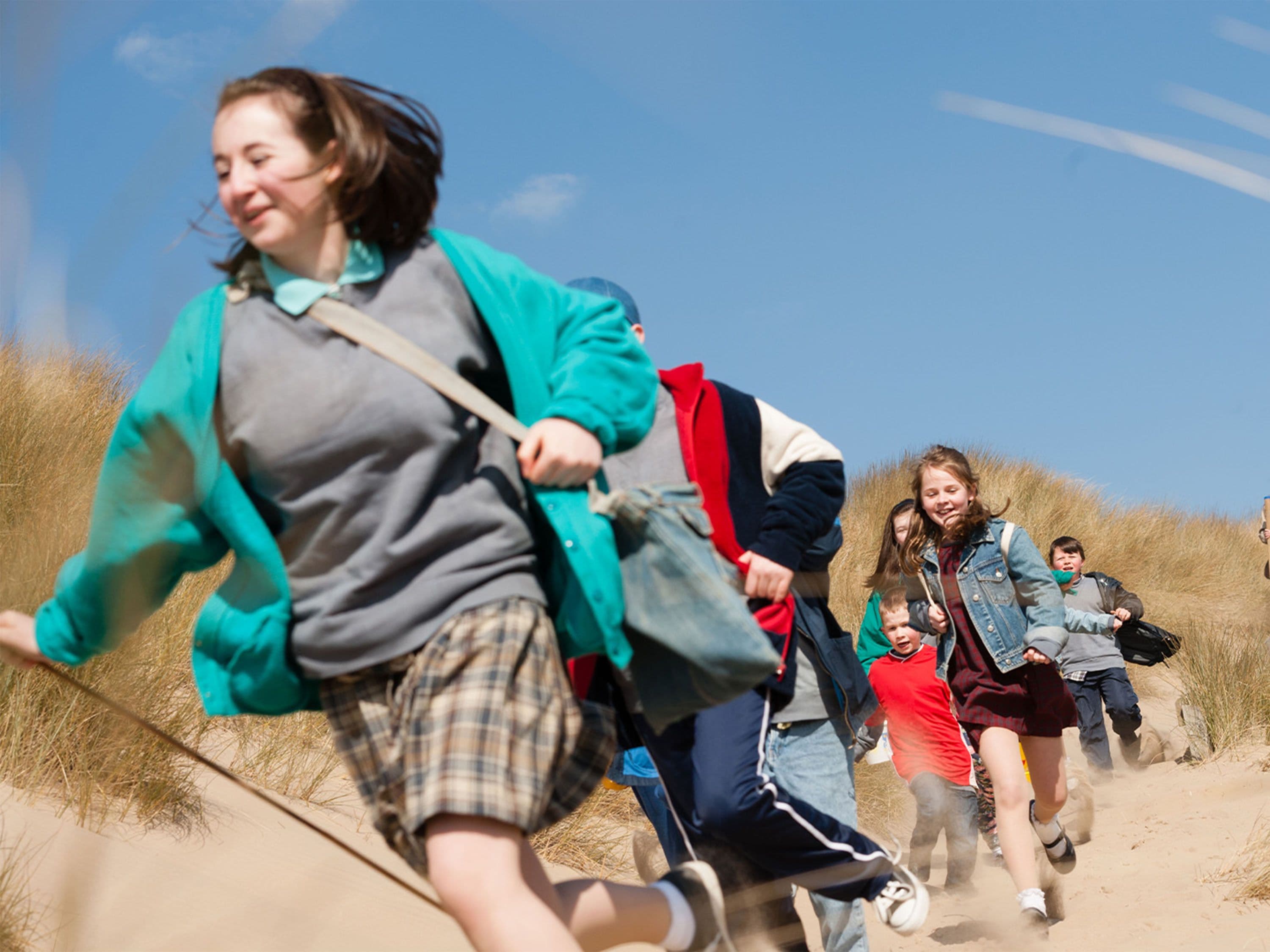 Jugendlichen, die einen sandigen Hang in einer Dünenlandschaft hinunterlaufen